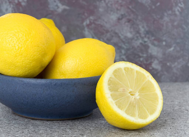 Een blauwe schaal van citroenen fruit op een tafel tegen een grijze marmeren achtergrond met kopieerruimte voor uw tekst - Foto, afbeelding
