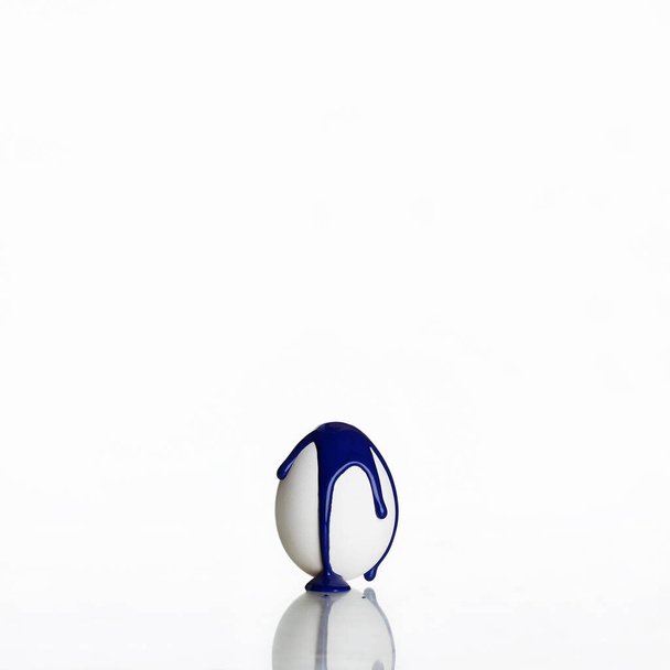 Paskalya yumurtası beyaz arka planda izole edilmiş. Mavi boya yumurtadan akıyor. minimalist poster - Fotoğraf, Görsel