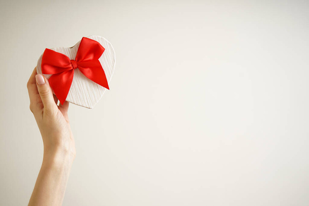 Manos femeninas con caja de regalo para el Día de San Valentín sobre fondo de color con espacio para texto. - Foto, imagen