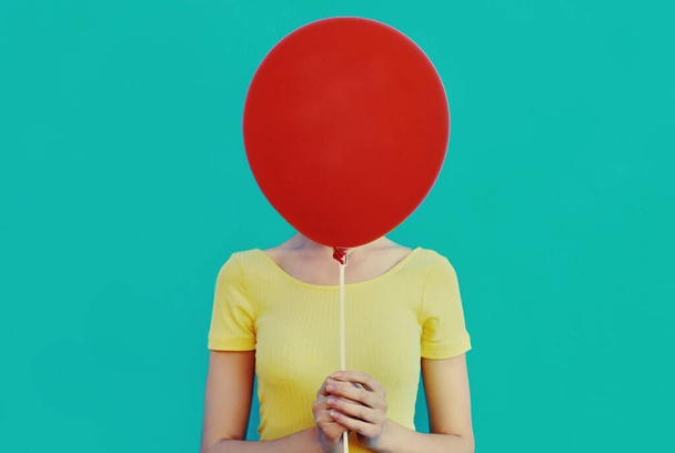 Portrait close up of woman covering her head with red balloon on a blue background - Foto, imagen