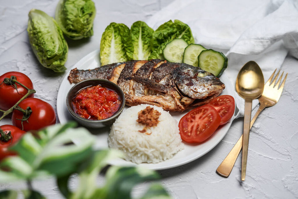 Pescado frito indonesio servido con arroz al vapor, verduras y sambal - Foto, Imagen
