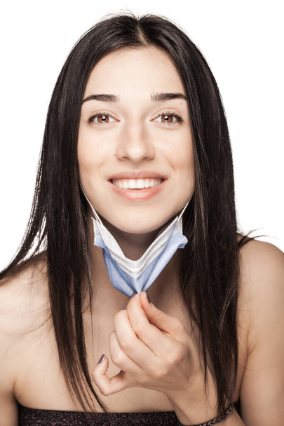 Happy girl pulling away medical face mask. Portrait against white background. - Foto, imagen