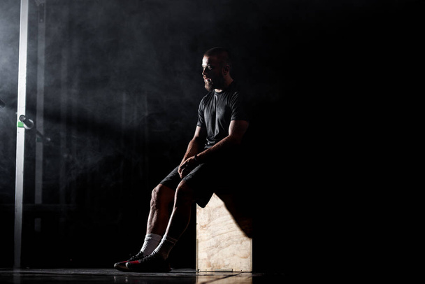 Silhouette of a muscular athlete posing in interior with weightlifting equipment. Smoke background. - Фото, зображення