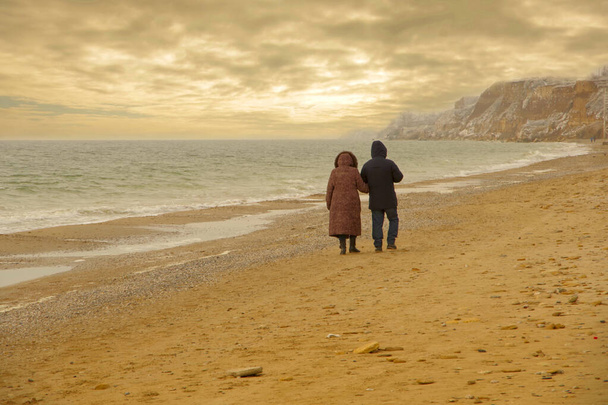 an elderly couple walking along a winter beach at sunset. - Photo, image