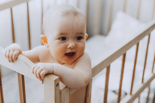 Candid shot of six month old infant baby  standing in the crib holding on to the side - Foto, Imagem