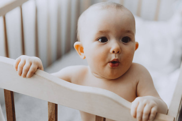 Candid shot of six month old infant baby  standing in the crib holding on to the side - Photo, image