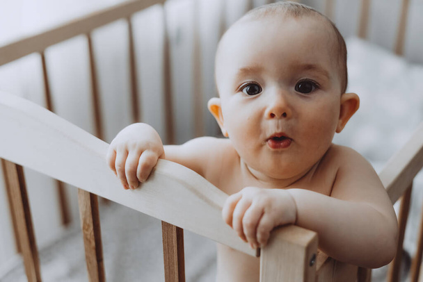 Candid shot of six month old infant baby  standing in the crib holding on to the side - Zdjęcie, obraz