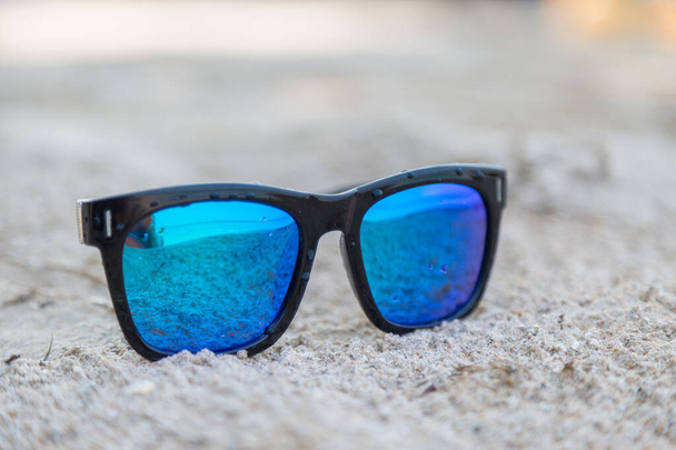 Gafas de sol azules sobre fondo de arena blanca - Foto, Imagen