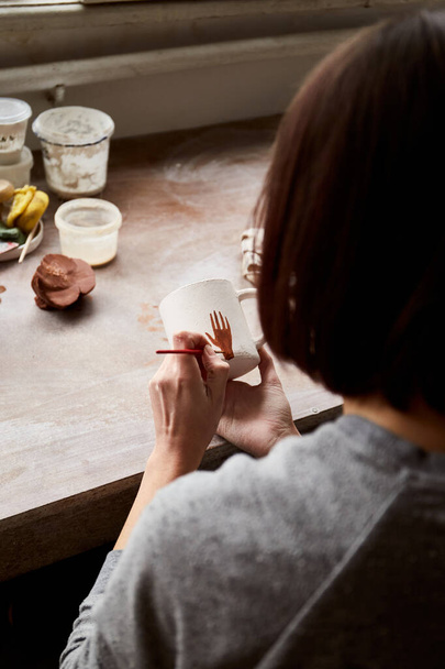 Vrouwelijke keramist werkzaam in aardewerk studio. Keramist 's handen vuil van klei. Proces van het maken van aardewerk. Master keramiste werkt in haar atelier - Foto, afbeelding