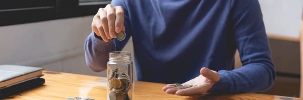 concetto di risparmio l'uomo con il maglione blu cercando di risparmiare i suoi soldi cadere le monete da dieci baht nella bottiglia.  - Foto, immagini