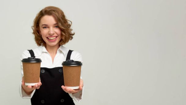 Coffee Business Concept - Beautiful caucasian lady smiling at camera offering disposable take away hot coffee - Photo, Image