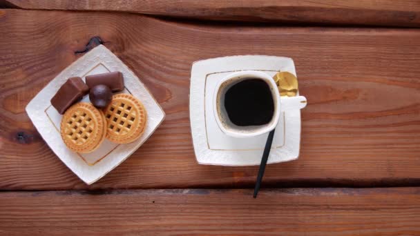 Steaming coffee with sweets on wooden table. Hot freshly brewed espresso coffee in white cup with steam. Crunchy cookies chocolate candies on plate top view. Restaurant drinks delicious breakfast menu - Footage, Video