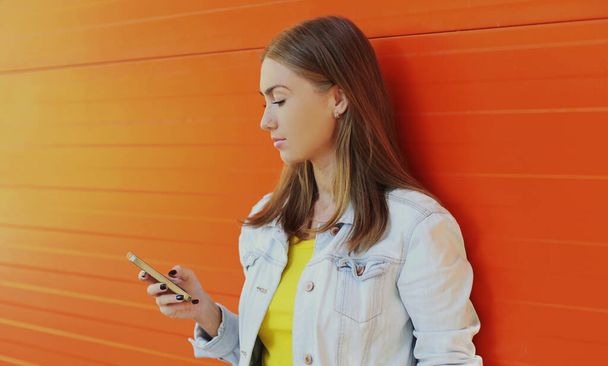 Portrait of modern young woman with phone in the city over an orange background - Fotografie, Obrázek