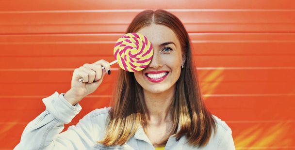 Summer colorful portrait of happy smiling young woman with lollipop over an orange background - 写真・画像