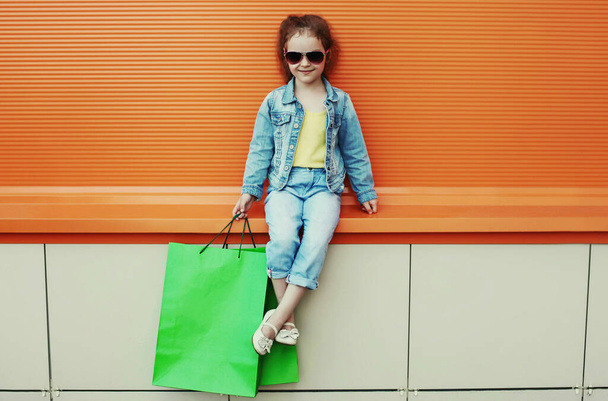 Portrait of little girl child posing with shopping bags wearing a denim clothes on a city street - Zdjęcie, obraz