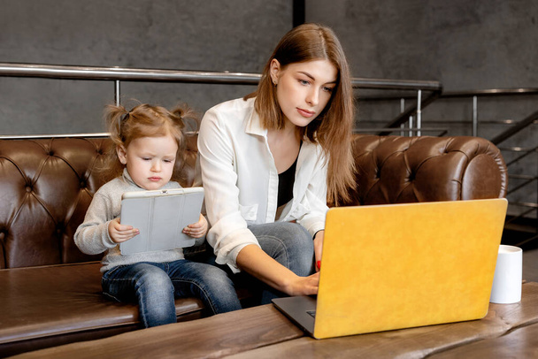 beautiful young mother with laptop  and her daughterwith tablet sitting on the sofa  - Foto, immagini