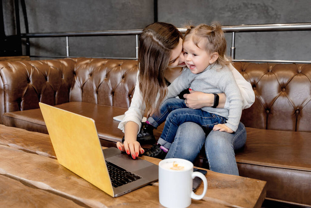 bela jovem mãe e sua filha sentada no sofá e usando laptop - Foto, Imagem