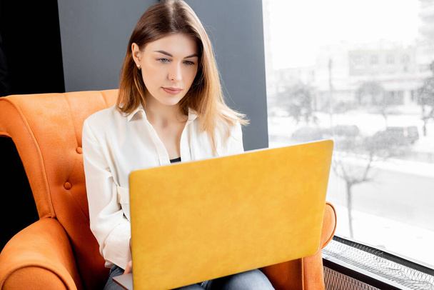 Dizüstü bilgisayarı olan genç bir kadın koltukta oturuyor.  - Fotoğraf, Görsel