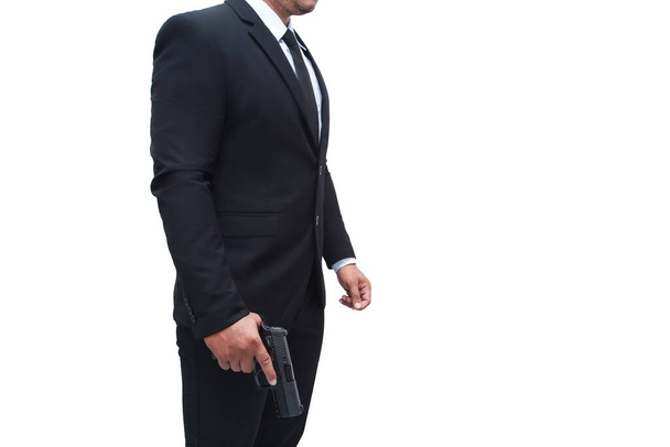 Vista lateral de un pistolero con un traje negro de pie con una pistola en una pose de popa, sobre un fondo blanco aislado. Concepto de asesino, asesinato, criminal. - Foto, Imagen