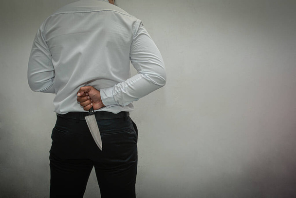 Knife killer. A man in a white shirt and black pants holding a knife behind his back. white background - Foto, Imagem
