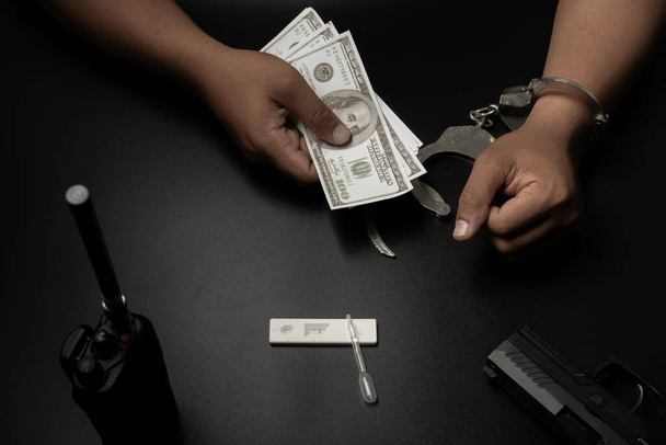 Ένας άντρας ήταν δεμένος με χειροπέδες σε ένα μαύρο τραπέζι. Εξετάζεται για ναρκωτικά. Τα αποτελέσματά του ήταν θετικά και έδωσε στην αστυνομία χρήματα για να τα δώσει. Διαφθορά, δωροδοκία, παράνομες συναλλαγές - Φωτογραφία, εικόνα