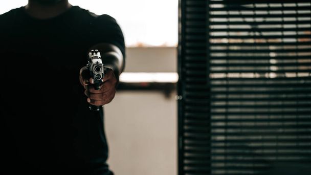 銃を持った黒シャツの犯罪者がドアを突破し、犯罪者の概念で彼の銃を目指す. - 写真・画像