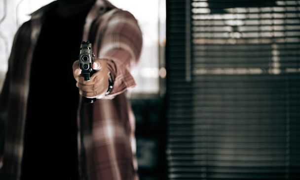 銃を持った縞模様のシャツを着た犯人がドアを突き破って犯人のコンセプトで銃を狙う. - 写真・画像