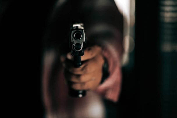Een crimineel in een gestreept shirt met een pistool breekt door de deur en richt zijn pistool op het criminele concept. - Foto, afbeelding