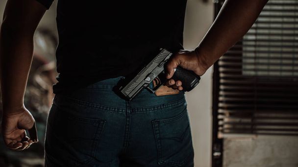 彼の背中の後ろに銃を持つ黒いシャツの泥棒は、強盗、強盗の概念を奪うために家のドアを突破. - 写真・画像