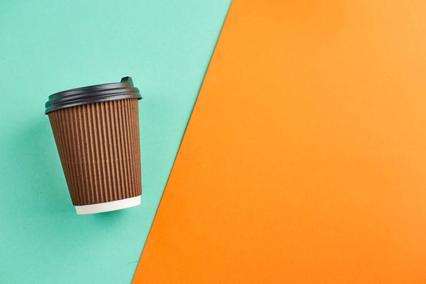 Paper coffee cup on orange and  turquoise background. Closeup blank craft paper coffee cup. Place for text. - Photo, Image