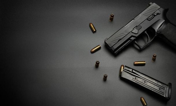 Le pistolet est placé sur un fond noir avec des balles de 9 mm tout autour. Idée pour arme à feu victime. - Photo, image