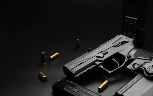 Die schwarze Pistole steht auf einem dunklen Hintergrund, um sie herum ist 9 mm Munition platziert. Und ein Polizeiradio mit Magzinen. Idee für Detektive. - Foto, Bild