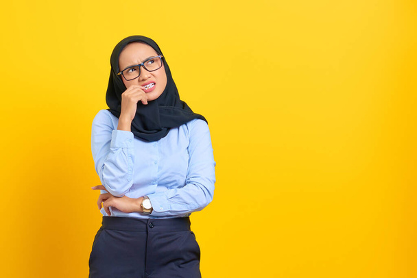 Portrait of pensive young Asian woman looking seriously thinking about a question isolated on yellow background - Photo, Image