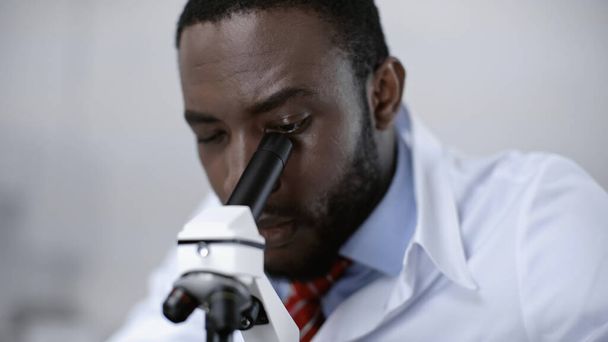 skoncentrowany amerykański naukowiec patrzący przez mikroskop w laboratorium klinicznym  - Zdjęcie, obraz