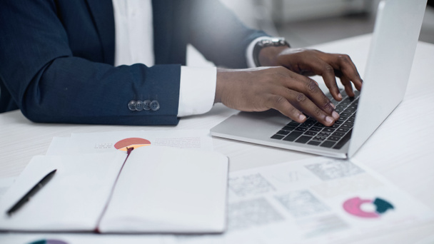 partial view of african american businessman using laptop near charts on desk  - Φωτογραφία, εικόνα