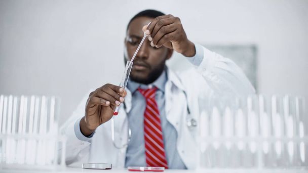 blurred african american scientist adding red liquid into test tube in lab - Photo, Image