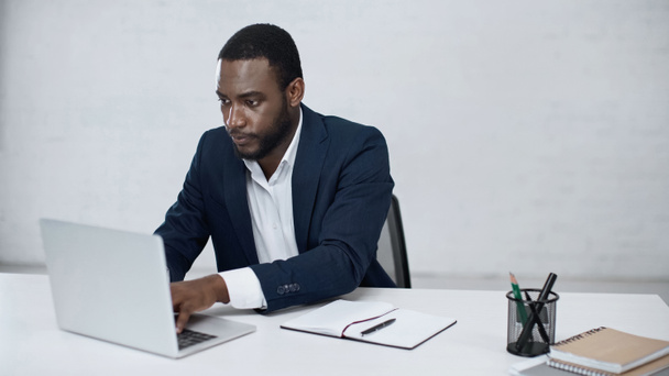 Ciddi bir Afro-Amerikan iş adamı Grey 'de dizüstü bilgisayarda yazıyor.  - Fotoğraf, Görsel