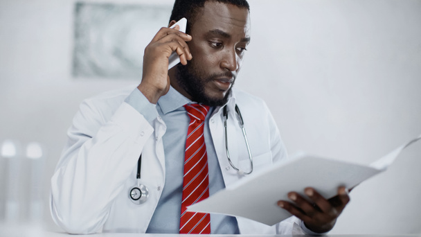 médecin afro-américain parlant sur smartphone tout en tenant dossier flou  - Photo, image