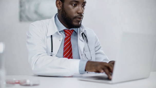 barbudo afroamericano médico escribiendo en el ordenador portátil en la clínica  - Foto, Imagen