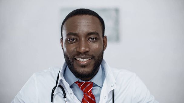 pozitivní africký americký lékař v bílém plášti na klinice - Fotografie, Obrázek