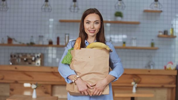 Uśmiechnięta kobieta trzyma w domu paczkę z jedzeniem  - Zdjęcie, obraz