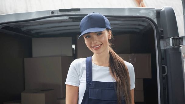 Happy delivery woman smiling at camera near car with packages outdoors  - Photo, Image