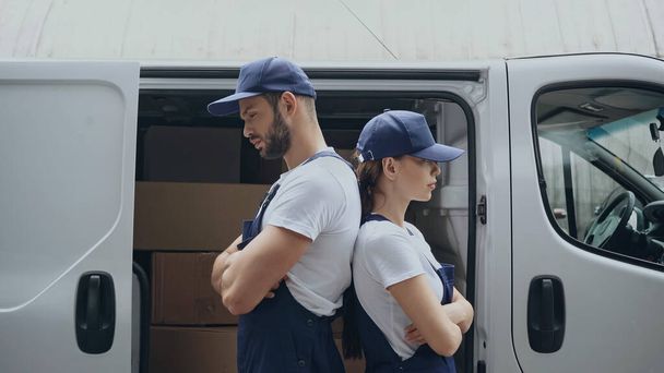 Side view of couriers standing back to back near car with carton boxes outdoors  - 写真・画像