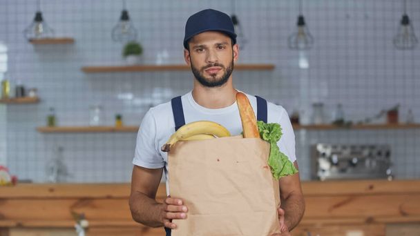Delivery man looking at camera while holding package with food at home  - Foto, Imagem