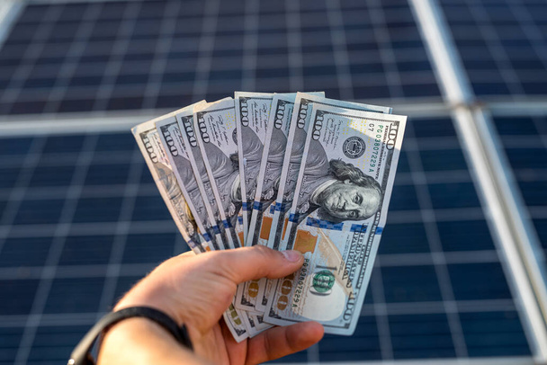 男性の手は代替エネルギーの生産による利益としてドルを保有しています。太陽電池パネル - 写真・画像
