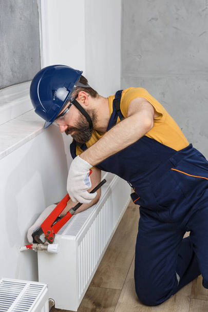 un operaio in un casco arancione installa radiatori in casa - Foto, immagini