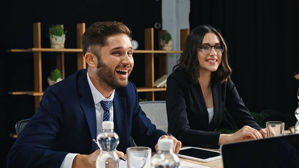Молодой бизнесмен смеется рядом с улыбающейся коллегой в зале заседаний - Фото, изображение