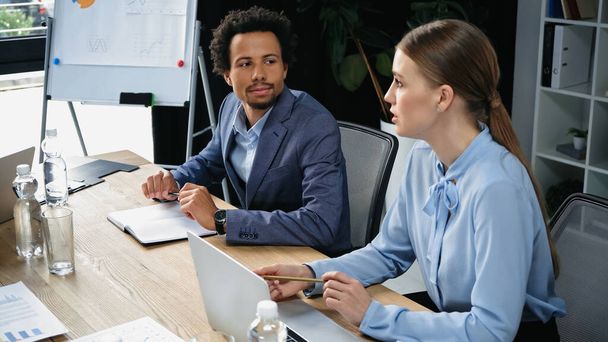 interracial business partners sitting near laptop and documents in meeting room - Φωτογραφία, εικόνα