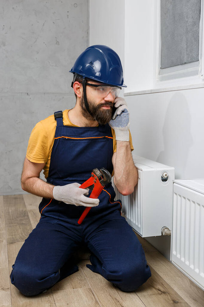 un trabajador en un casco naranja instala radiadores en la casa - Foto, imagen