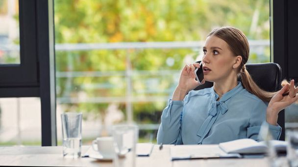 young businesswoman talking on mobile phone in office on blurred foreground - Foto, Imagen
